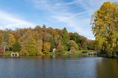 Wiltshire 'daki Stourhead bahçesindeki gölün etrafındaki sonbahar renklerinin görüntüsü.