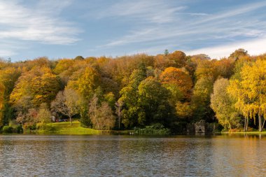 Wiltshire 'daki Stourhead bahçesindeki gölün etrafındaki sonbahar renklerinin görüntüsü.