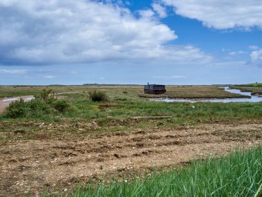 Brancaster Marsh 'ta bir ev teknesi, Kuzey Norfolk kıyısında Burnham Deepdale yakınlarında. Ufukta yürüyen yürüyüşçüler ve ufukta Royal West Norfolk Golf Kulübü var..