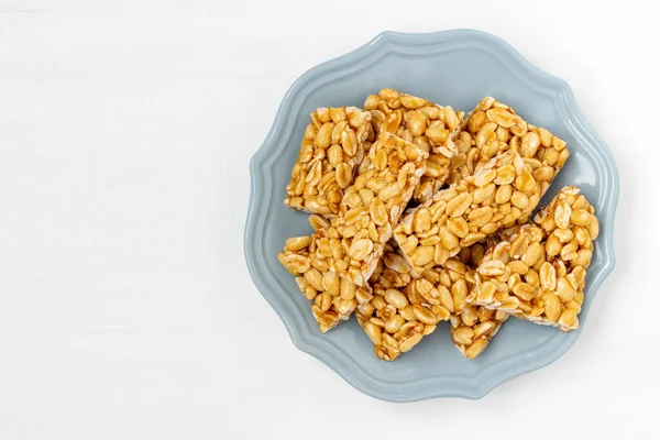 Plate of peanut brittle candy pieces. Top view on a white wooden background.