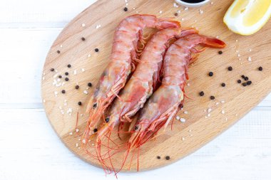 Donmuş büyük karidesler (langoustines), ahşap tahtada limon ve baharatlar. Deniz ürünleri pişirmek için gerekli malzemeler