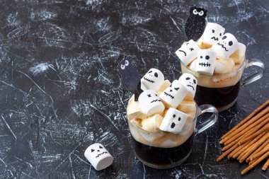 Marşmelovlu iki fincan kahve (ürkütücü yüzler, canavar, yarasalar). Karanlık arka planda Cadılar Bayramı yemeği. Kutlama konsepti