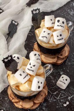Esmer arka planda iki fincan marshmallow (ürkütücü yüzler, canavar, yarasalar). Cadılar Bayramı yemeği