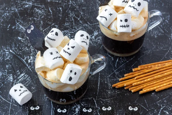 Creepy faces (monster) from marshmallows in cup of coffee. Halloween food on dark background. Festive concept