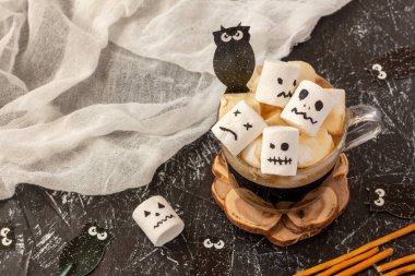 Cadılar Bayramı için bir fincan kahvenin içinde kremalı şekerlemelerden ürkünç yüzler. Şenlik konsepti. Boşluğu kopyala