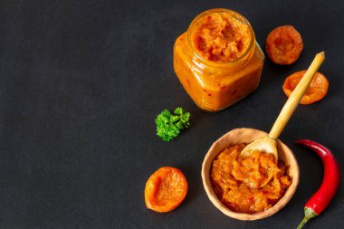 Geleneksel baharatlı, kurutulmuş kayısı turşusu ve siyah arka planda cam kavanozda acı biber. Sonbahar ve kış mevsimi için saklanmış lezzetli vejetaryen tatlı baharatlı sos. Boşluğu kopyala