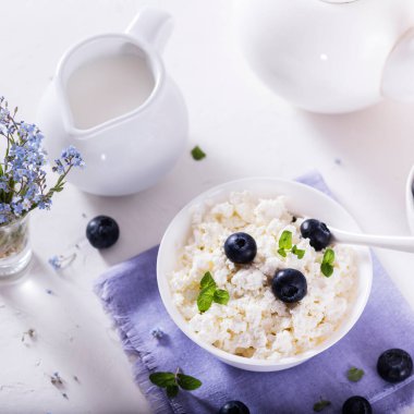 Beyaz kâse içinde sağlıklı kahvaltı süzme peyniri ve taze yaz meyveleri.