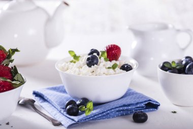 Beyaz kâse içinde sağlıklı kahvaltı süzme peyniri ve taze yaz meyveleri.