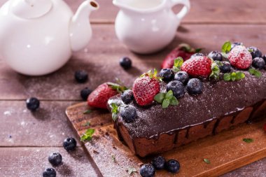 Taze lezzetli ev yapımı çikolatalı pasta ve ahşap bir masada yaz meyveleri..