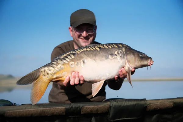 Mutlu gülümseyen balıkçı, arka planda göllü balığını tutuyor. Sazan balığına odaklan.