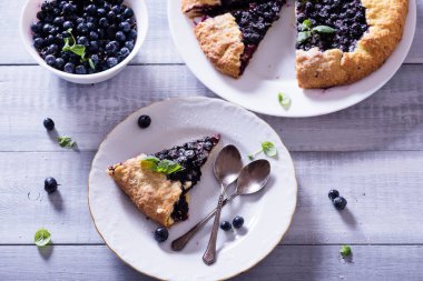 Ev yapımı çıtır yaban mersinli turta veya galette ve nane. Yaz, parlak, lezzetli turtalar çiçeklerle çerçevelenmiş ve böğürtlenli otlar