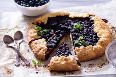 Ev yapımı çıtır yaban mersinli turta veya galette ve nane. Yaz, parlak, lezzetli turtalar çiçeklerle çerçevelenmiş ve böğürtlenli otlar