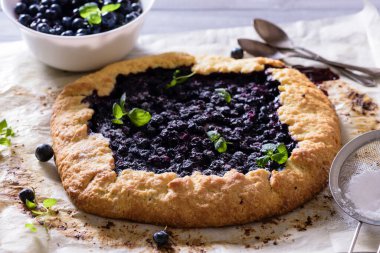 Ev yapımı çıtır yaban mersinli turta veya galette ve nane. Yaz, parlak, lezzetli turtalar çiçeklerle çerçevelenmiş ve böğürtlenli otlar