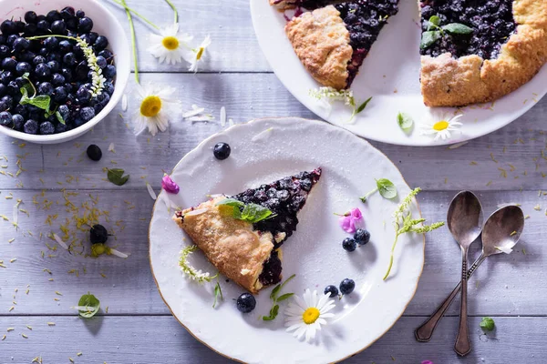 Ev yapımı çıtır yaban mersinli turta veya galette ve nane. Yaz, parlak, lezzetli turtalar çiçeklerle çerçevelenmiş ve böğürtlenli otlar