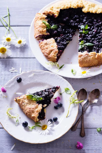 Ev yapımı çıtır yaban mersinli turta veya galette ve nane. Yaz, parlak, lezzetli turtalar çiçeklerle çerçevelenmiş ve böğürtlenli otlar