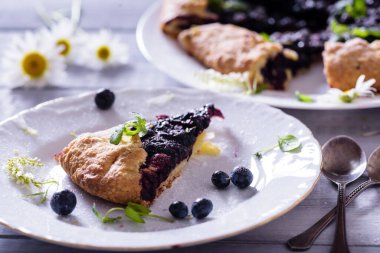 Ev yapımı çıtır yaban mersinli turta veya galette ve nane. Yaz, parlak, lezzetli turtalar çiçeklerle çerçevelenmiş ve böğürtlenli otlar