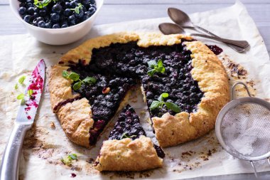 Ev yapımı çıtır yaban mersinli turta veya galette ve nane. Yaz, parlak, lezzetli turtalar çiçeklerle çerçevelenmiş ve böğürtlenli otlar