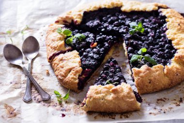 Ev yapımı çıtır yaban mersinli turta veya galette ve nane. Yaz, parlak, lezzetli turtalar çiçeklerle çerçevelenmiş ve böğürtlenli otlar