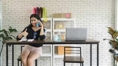 Tüccar. Genç, modern bir Asyalı kadının internette satış kariyeri var. Telefonda konuşmak, müşterilerden emir almak ve notlar almak. İletişim teknolojisini ve interneti pazarlamak için kullanıyor.