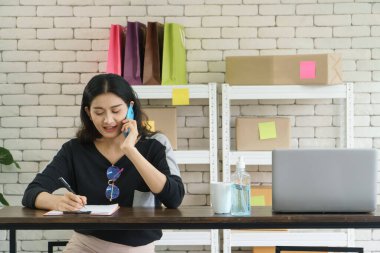 Tüccar. Genç, modern bir Asyalı kadının internette satış kariyeri var. Telefonda konuşmak, müşterilerden emir almak ve notlar almak. İletişim teknolojisini ve interneti pazarlamak için kullanıyor.