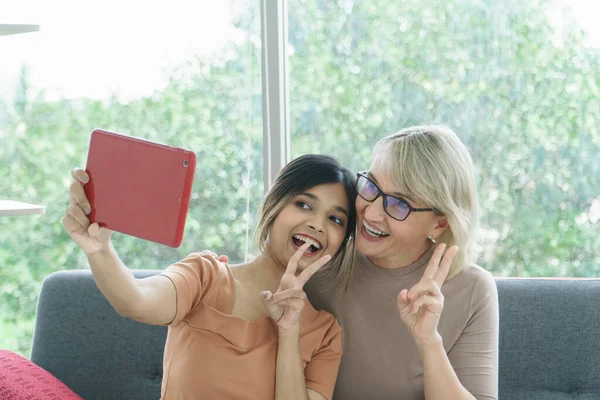 Derisi karışık mutlu bir aile. Torun ve büyükanne evde teknolojiyi ve eğlenceyi paylaşıyor. konsept, cilt sevgisi, bakım büyükanne, anne ve kız, üvey anne veya üvey kız evlatlık.