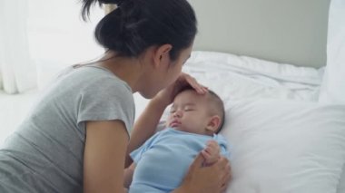 Genç Asyalı anne, bebek alnını öperken, bebek odasında yeni doğmuş bir kızın yatakta uyuduğunu görür. Bebek Kavramları, Ebeveynlik, Çocukluk Hayatı, Aşk, Kibarca Sarılma