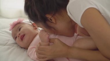 Genç Asyalı Anne Sevimli Bebek Kızıyla Oynuyor Sevgi ve şefkatle yanakları öpüyor. Yeni doğmuş kız bebek tatlı ve neşeli. konsept annelik çocuk yetiştirme kreş sevgi ve aile hayatında