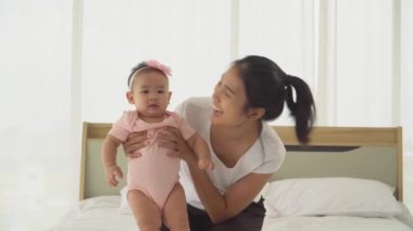 Genç Asyalı Anne Sevimli Bebek Kızıyla Oynuyor Sevgi ve şefkatle yanakları öpüyor. Yeni doğmuş kız bebek tatlı ve neşeli. konsept annelik çocuk yetiştirme kreş sevgi ve aile hayatında