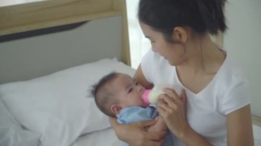 Genç Asyalı anne küçük kızını kucağında tutuyor ve biberonla besleniyor. Yeni doğmuş bebek, annelik, aşk, aile kavramı dışında bebek şişesiyle beslenmek.