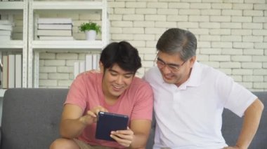 Büyük baba ve büyüyen oğul tablet tutarlar, komik şakalar yaparlar ve mutlu bir şekilde gülerler. Mutluluk kavramı, Asyalı aile, aşk, aile ilişkisi.