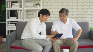 Mutlu kıdemli baba ve büyüyen oğul dijital tabletlere bakıp konuşuyorlar. Emekliler teknolojiyi gençlerle birlikte kullanmayı öğreniyorlar. konsept, aile zaman paylaşımı, iyi ev ilişkisi