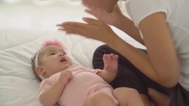 Mutlu Asyalı genç anne yatak odasında küçük kızıyla oynuyor. Sevimli, sağlıklı, neşeli bir kız bebek yatakta uzanıyor ve gülümsüyor. Annelik kavramları, ebeveynlik, aile hayatı, çocuk bakımı.