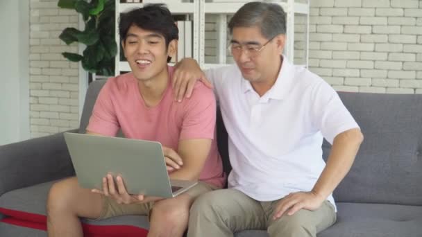 幸せな高齢者の父と成長している息子が話しているとノートパソコンを見ています 退職者は若い男性と技術を使用することを学んでいる コンセプト 家族時間の共有 良い家庭関係 — ストック動画