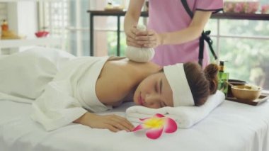 Güzeller güzeli Asyalı kadınları spa salonunda yatakta yatırmak. Tayland masajı yapan genç bir kadın. Kadın omzuna ve sırtına masaj yapmak için bitkisel kompres kullanan masöz el. Kadın fikirleri için masaj ve spa