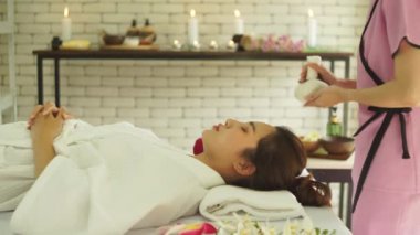 Güzeller güzeli Asyalı kadınları spa salonunda yatakta yatırmak. Tayland masajı yapan genç bir kadın. Masöz el bitkisel kompres kullanıyor. Kadının alnına masaj yap. Fikirler kadınlar için masaj ve spa