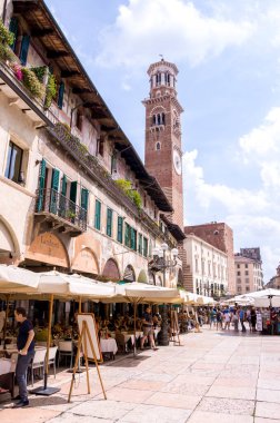 İtalya, Verona 'daki Piazza delle Erbe' nin arka planında insanlar ve Lamberti Kulesi olan kafe.