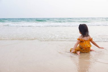 Asyalı kız plajda denize bakarak kum üzerinde oturan