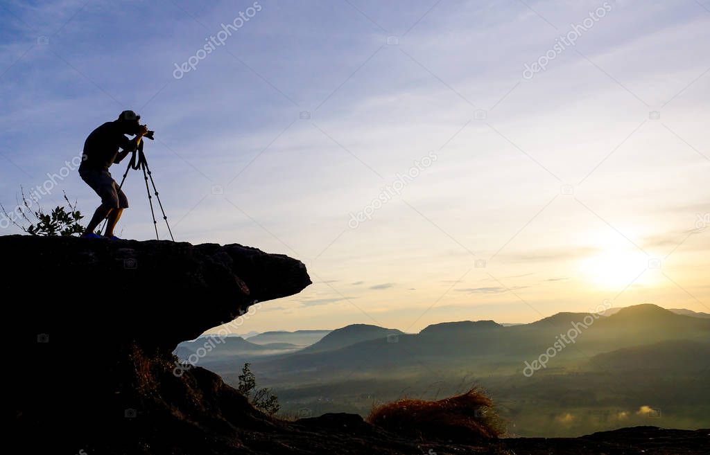 A photographer standing on a cliff, taking a photo of a sunrise silhouette