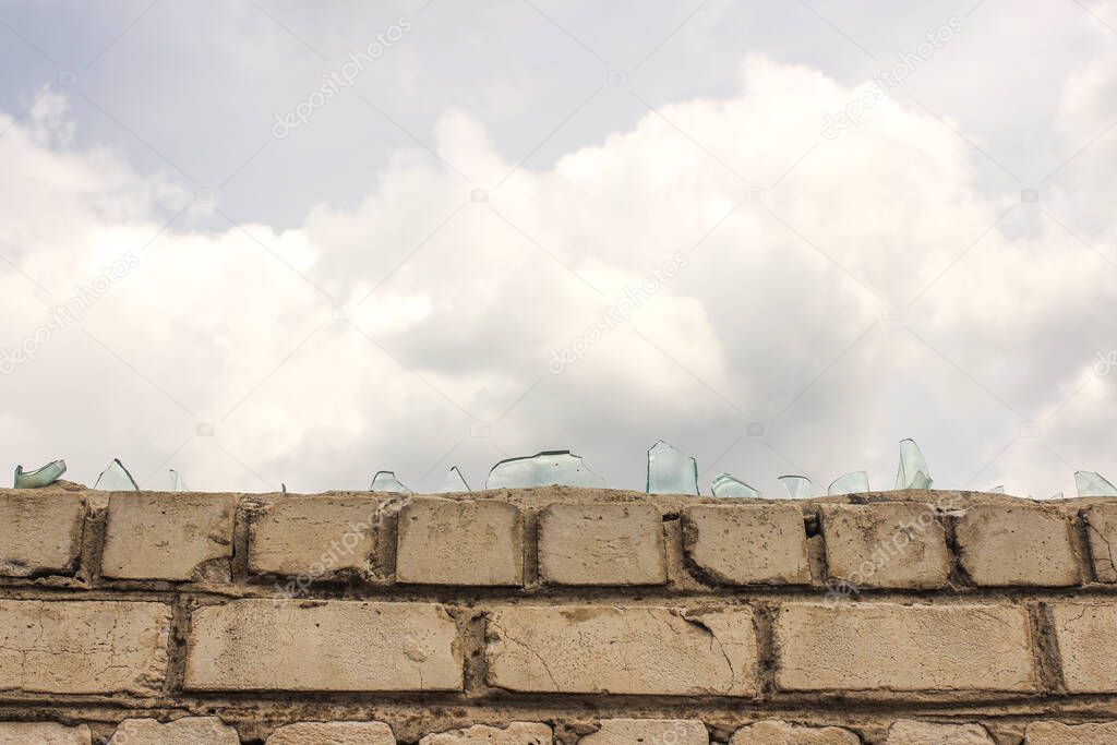 Glass of broken bottles on a brick fence against vandals against a blue sky