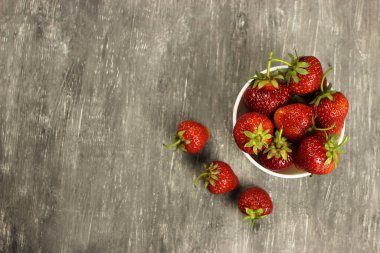 Çilekler, gri arka planda bir tabakta olgunlaşmıştı.