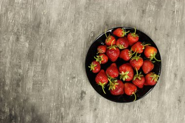Çilekler, gri arka planda bir tabakta olgunlaşmış, üst manzara. Boşluğu kopyala