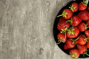 Çilekler, gri arka planda bir tabakta olgunlaşmış, üst manzara. Boşluğu kopyala