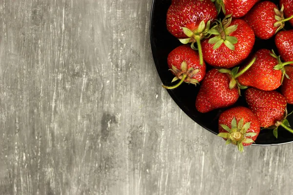 Çilekler, gri arka planda bir tabakta olgunlaşmış, üst manzara. Boşluğu kopyala