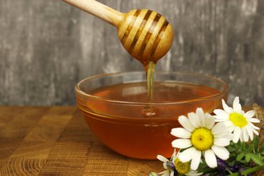 Çubuklu bir kasede bal ve tahtanın üzerinde yabani çiçekler