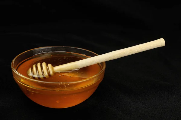 Honey in a bowl with a wooden stick on a black background