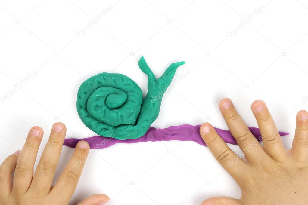 A child sculpts a snail from modeling clay, plasticine