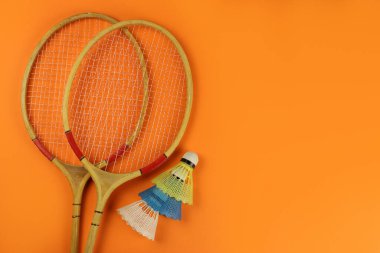 parlak turuncu arka planda badminton raketleri ve mekikleri