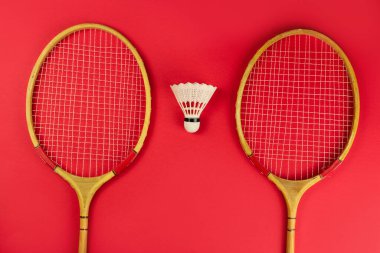 badminton raketleri ve parlak kırmızı arka planda bir mekik.