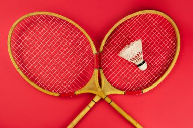 badminton raketleri ve parlak kırmızı arka planda bir mekik.