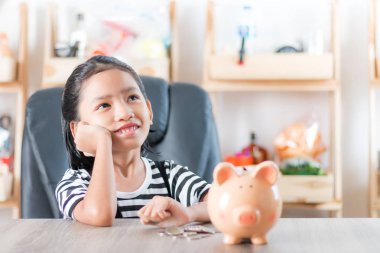 Asian little girl in looking up and dreaming with piggy bank metaphor planning for save money shallow depth of field select focus at the pig clipart